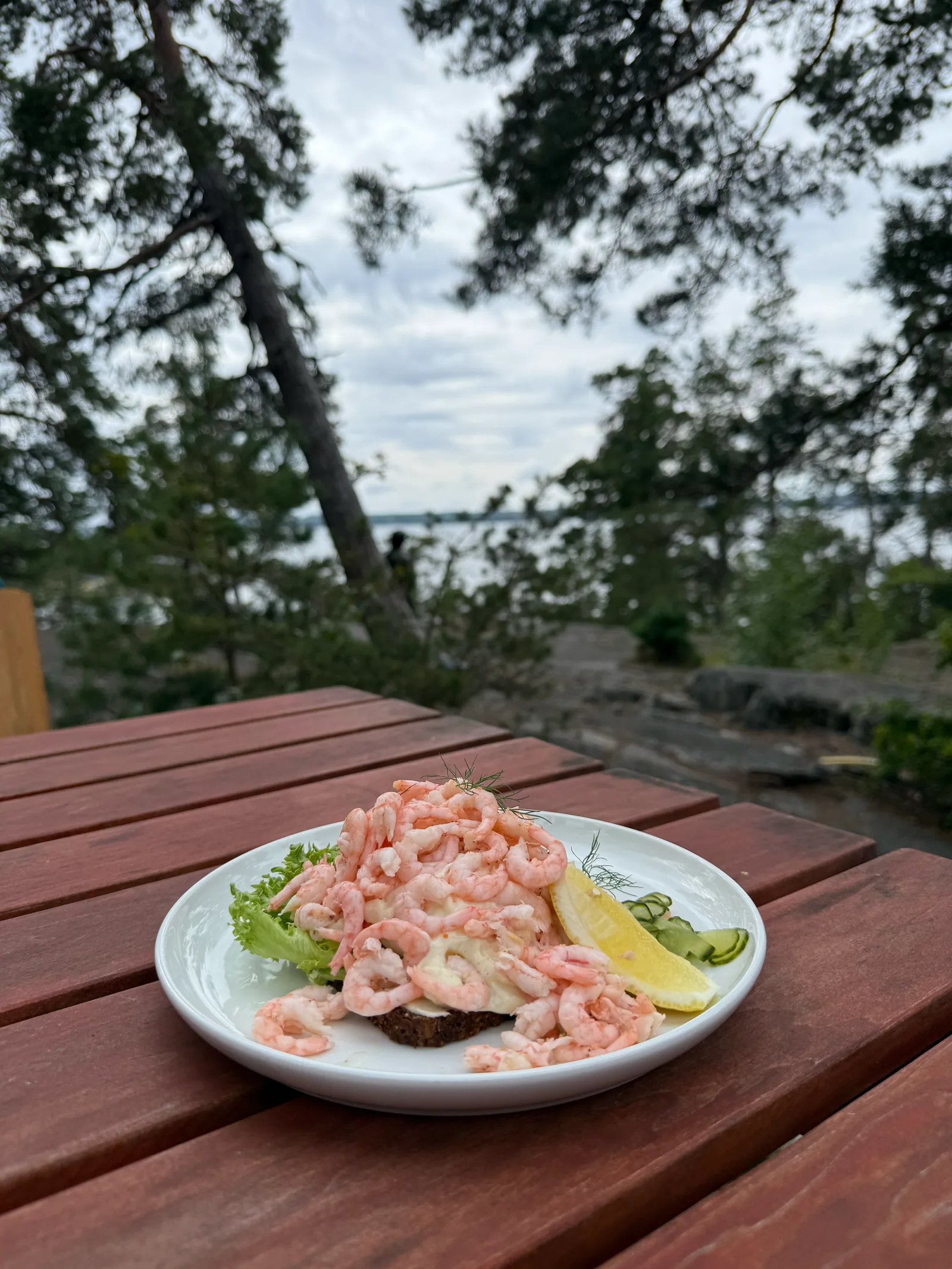 Räksmörgås mit Nordmeergarnelen und Zitrone auf einem roten Holztisch am Wasser