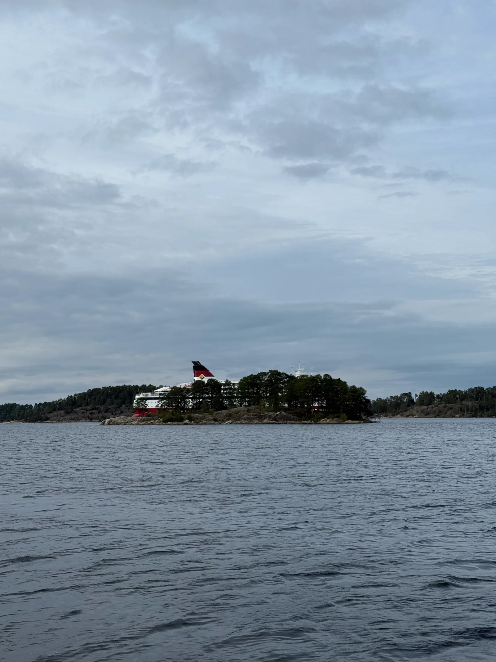 Große Ostseefähre fährt hinter einer bewaldeten Schäreninsel vorbei