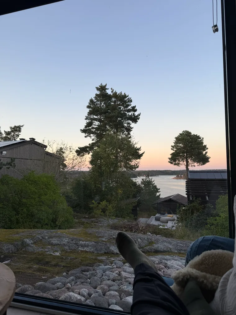 Blick aus einem Fenster auf Bäume und Wasser bei Sonnenuntergang