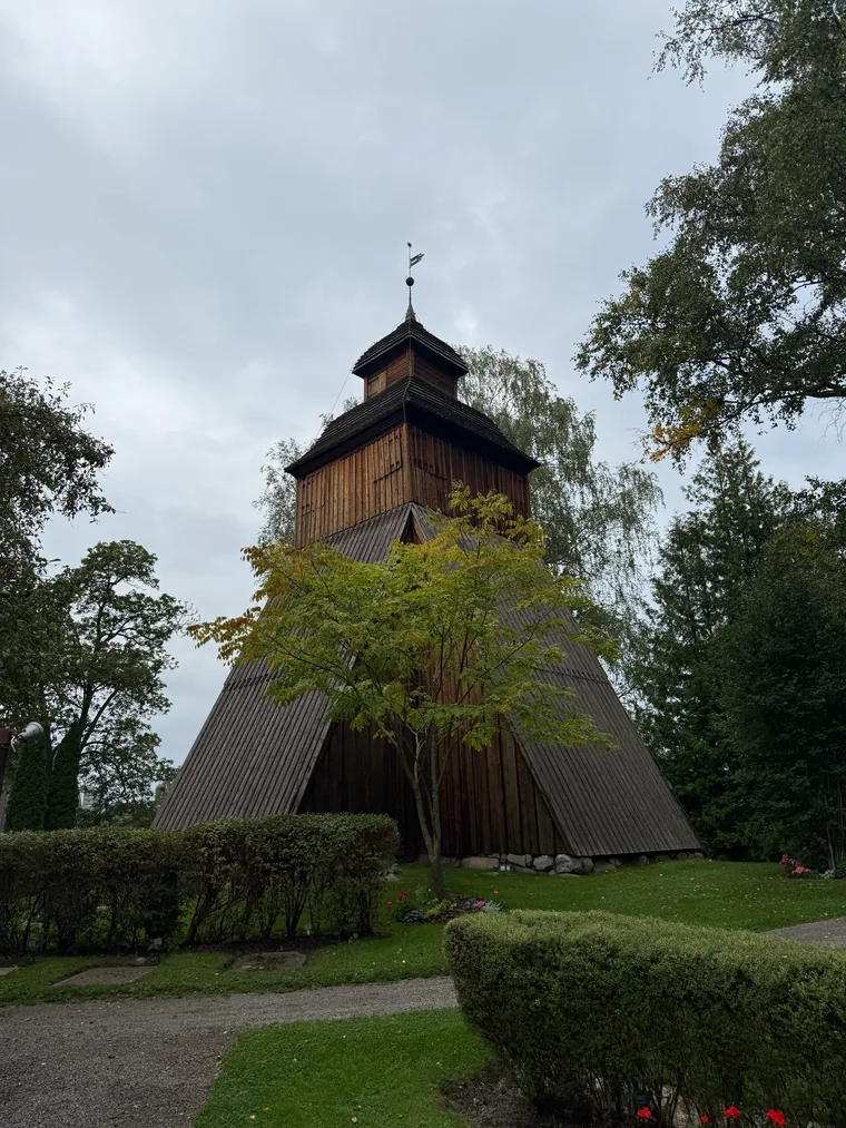 Freistehender hölzerner Glockenturm mit geteerter Verschalung neben einer Kirche