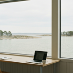 Heller Coworking-Arbeitsplatz mit Laptop an einem großen Fenster mit Blick auf das ruhige Wasser und die Granitschären bei Stockholm