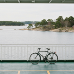 Fahrrad neben der Reling einer Stockholmer Schaerenfaehre mit flachen Granitinseln und rotem Holzhaus im Hintergrund