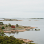 Entlegene äußere Schäreninsel mit wenigen falunroten Häusern und kleinem Holzsteg an der ruhigen Ostsee