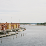 Hafenfront von Sandhamn mit großen gelben und roten Holzgebäuden, Steganlage und vertäuten Booten im Schärengarten