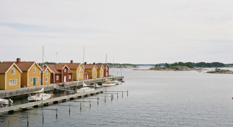Hafenfront von Sandhamn mit großen gelben und roten Holzgebäuden, Steganlage und vertäuten Booten im Schärengarten