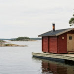 Rot gestrichene schwimmende Holzsauna an einem Holzsteg in den Stockholmer Schären, ruhige Ostsee und flache Granitfelsen