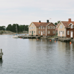 Traditionelle schwedische Holzhaeuser an der Hafenfront von Vaxholm mit Steg, kleinen Booten und ruhiger Ostsee