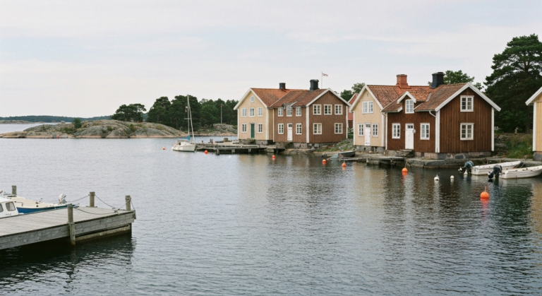 Traditionelle schwedische Holzhaeuser an der Hafenfront von Vaxholm mit Steg, kleinen Booten und ruhiger Ostsee