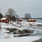 Falunrote Schaerenhaeuser mit weissen Fensterrahmen im Schnee, schneebedeckter Granit und teils vereiste Ostsee